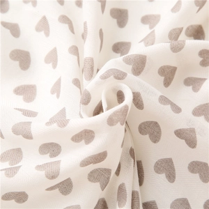 Close-up of soft beige cotton linen scarf featuring a recurring taupe heart print pattern