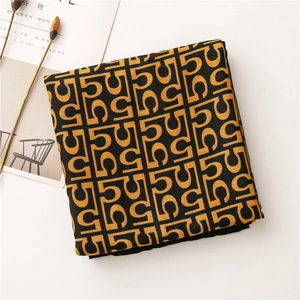 Close-up of folded cotton linen scarf with orange geometric letter pattern on black