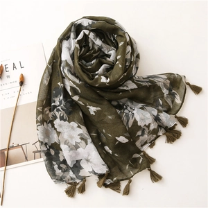 Detail of dark olive green floral scarf with white flowers and tassel edges on white background