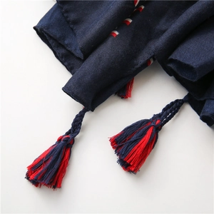 Dettaglio della sciarpa blu scuro con trama twill e nappe intrecciate rosso-blu