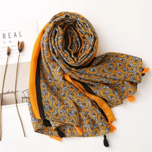 Detail view of the orange cotton-linen scarf with floral patterns and tassel edges
