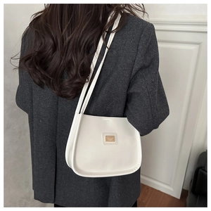 Close-up of cream leather shoulder bag with golden logo plate on grey blazer outfit