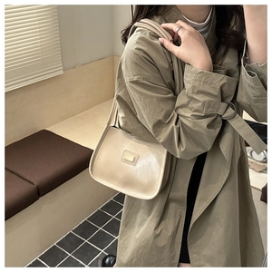 Detail of minimalist beige PU leather shoulder bag with gold hardware on a beige trench coat