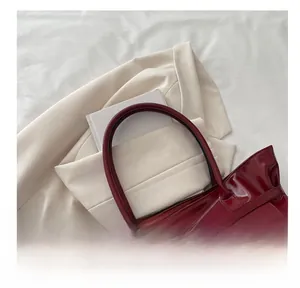 Vue détaillée du sac cabas en cuir verni rouge foncé avec texture brillante et anse ronde