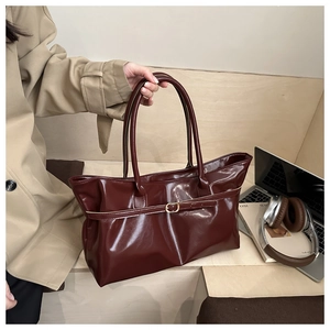 Détail du cabas en cuir verni bordeaux avec boucle métallique dans un décor de bureau