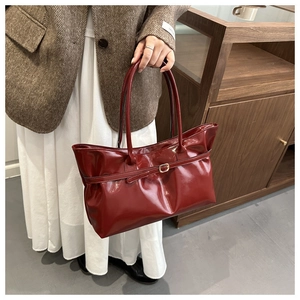 Gros plan du sac cabas en cuir brillant rouge foncé avec boucle dorée et détail de ceinture