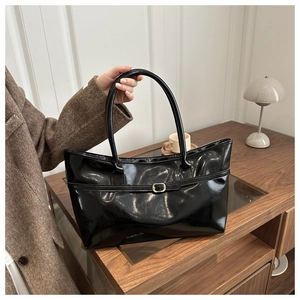 Détail d'un sac cabas noir brillant avec boucle dorée et fines anses de transport