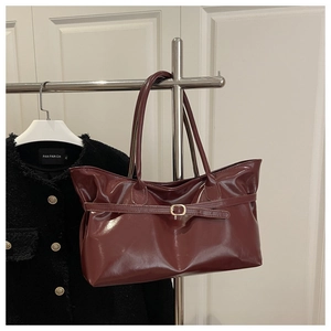 Détail du cabas en cuir verni bordeaux brillant avec boucle métallique sur un cintre