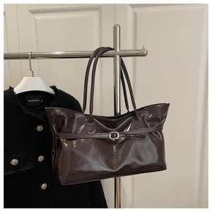 Détail d'un cabas en cuir verni chocolat brillant avec boucle dorée sur un support