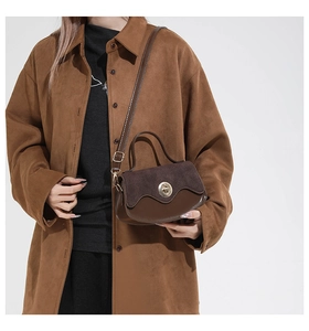 Dettaglio borsa scamosciata marrone con chiusura a rotazione dorata e bordo in pelle a onde