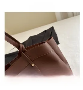 Close-up of caramel leather tote bag detailing golden metal charm and stitching