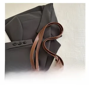 Detail of brown leather tote bag showing handle and gold metal ring decorative accents