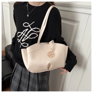 Close-up of cream white tote bag with gold M-letter charm and elegant wavy edges