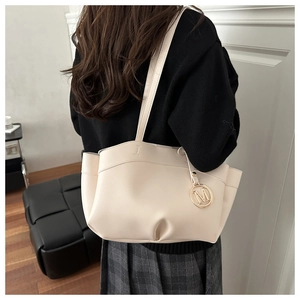 Detail showing cream-white tote bag with gold M-charm and pleated texture on model