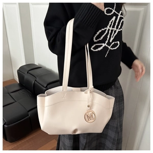 Close-up of cream tote bag featuring a gold M-letter pendant and smooth leather texture
