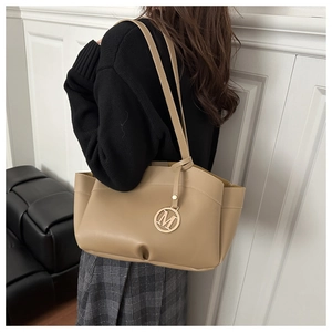 Detail of khaki tote bag with round gold M pendant shown on model in modern setting