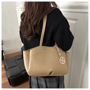 Detailed view of khaki leather tote bag featuring a decorative golden M letter charm