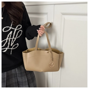Detail of beige tote bag with embossed I-letter and metallic M-pendant charm