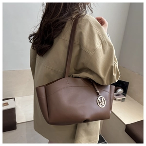 Detail view of a brown leather tote bag with a golden metal letter M charm and shoulder strap