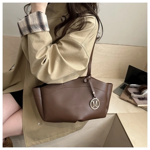 Detailed view of deep brown leather tote bag with metallic M charm in a lifestyle setting