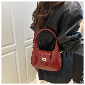 Detail of glossy red patent leather handbag with gold metal clasp on black leather outfit