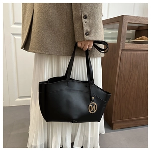 Detailed shot of a black leather tote bag featuring a golden M-letter metal pendant charm