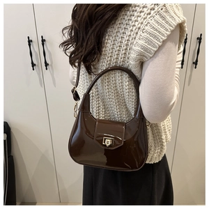Detail of dark brown patent leather dumpling bag with gold twist lock and shoulder strap