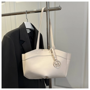 Close-up of cream tote bag with stylish metallic 'M' pendant and smooth faux leather texture