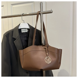 Detailed view of dark brown tote bag with gold round M pendant on silver hanger