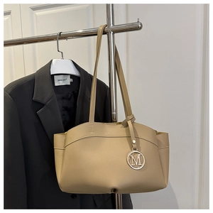 Detail of light khaki tote bag with a metallic M pendant and premium matte leather texture