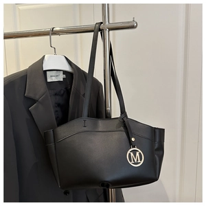 Detail of black tote bag with gold M pendant hanging on a metal rack next to a blazer