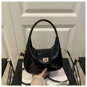 Detail of glossy black patent leather dumpling bag with gold metal buckle and handle
