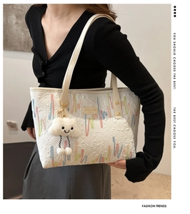 Detail view of white textured tote bag with colorful embroidery and a plush cloud charm
