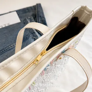 Detail of smooth gold metal zipper closure on striped tote bag with colorful embroidery