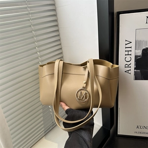 Large beige leather tote bag for women with elegant M charm pendant in a modern indoor setting