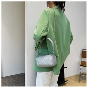 Détail du sac cylindrique argenté pailleté avec bandoulière chaîne sur un blazer vert