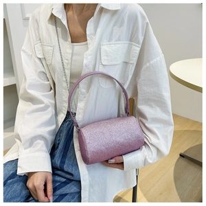 Détail d'un sac cylindrique rose pailleté avec bandoulière chaîne sur chemise blanche