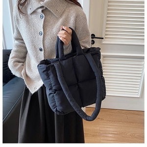 Detail of a black quilted puffy tote bag featuring soft square textured stitching