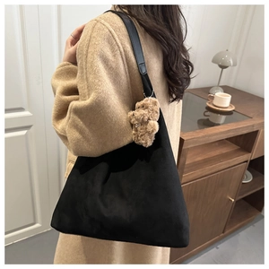 Detail of black suede tote bag with cute brown plush bear charm worn by a model