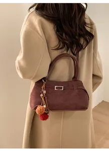 Detail of burgundy faux suede tote bag with pompom charm on beige coat