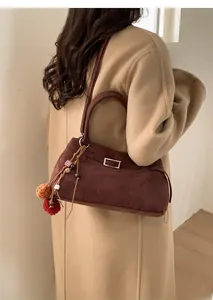 Detail of dark brown faux suede tote bag with boho pompom charm and metal buckle accent