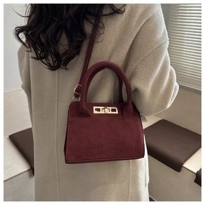 Detail of burgundy faux suede handbag featuring gold twist-lock and matching shoulder strap