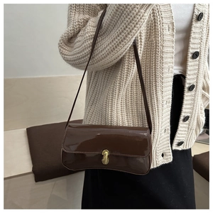 Dettaglio borsa a spalla in vernice marrone con chiusura dorata indossata da una modella