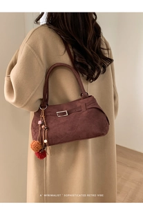 Detail of dark brown suede tote bag with colorful pom-pom charm and metal buckle