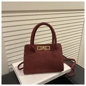 Detail of burgundy matte suede handbag with golden rectangular metal twist lock and handle
