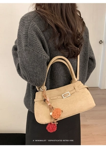 Detail of khaki suede tote bag with metal buckle and colorful pompom bag charm