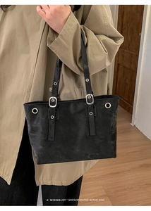 Close-up of black tote bag with silver square buckles and metallic eyelet details