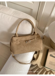 Detail of camel suede tote bag with retro buckle and adjustable strap on a sofa