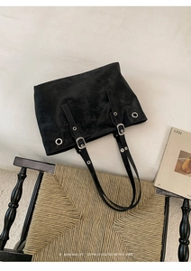 Close-up of black suede tote bag with silver buckle details on a vintage chair
