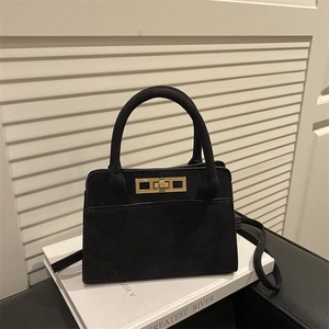 Vintage black matte handbag with gold lock on books against a white shutter wall